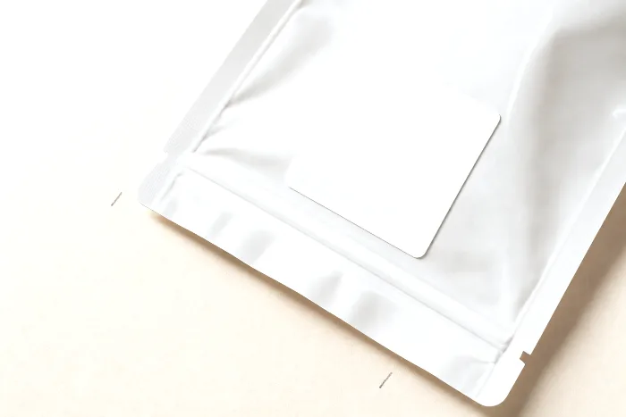 Close-up of a clear poly bag laid flat with a heat-sealed edge, a blank white label square, and pencil tick marks beside its opening.