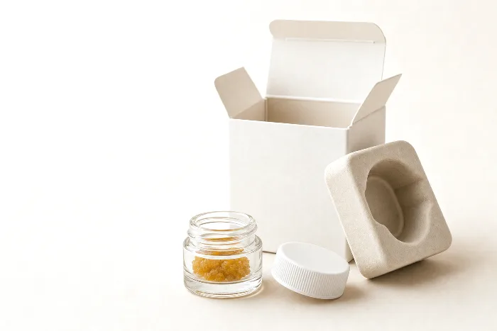 Tiny blank glass concentrate jar with child-resistant lid off, beside a small blank open carton with a fitted pulp insert.