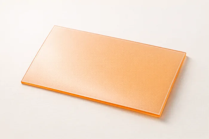 A translucent amber photopolymer flexographic printing plate resting at an angle, its relief surface catching the light.