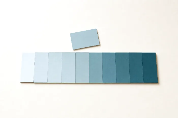 A row of small teal paper cards in slightly different shades on warm paper, one card set apart above the line.