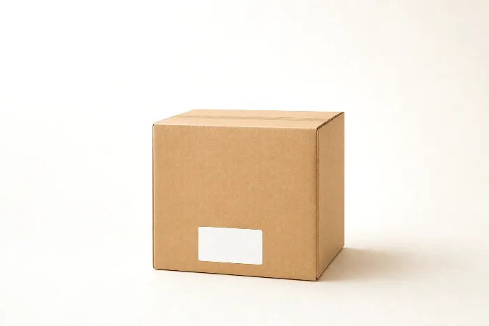 Sealed blank kraft case with a blank white label on its front panel, a corner board leaning against it, and a blank placard card in front.