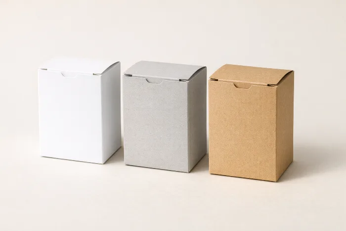 Three identical blank folding cartons in white SBS, gray recycled CRB, and brown kraft CUK paperboard.