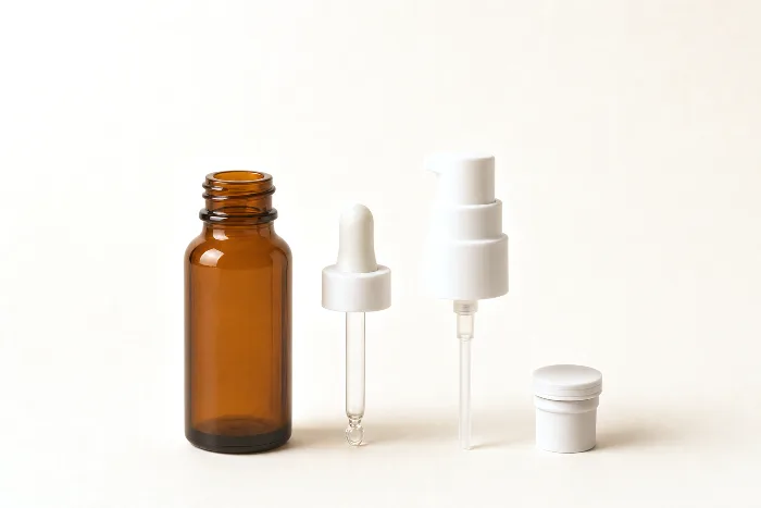 Amber glass bottle with a glass dropper pipette, a pump with long dip tube, and an airless piston part laid out beside it.