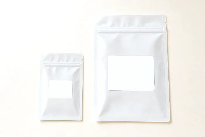 A small and a large clear poly bag laid flat, each with a blank white label rectangle sized in proportion to its bag.