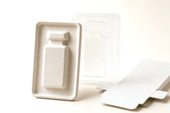 Blank molded pulp insert with an empty cartridge-shaped pocket, a clear thermoformed blister shell behind it, and a flat carton blank.